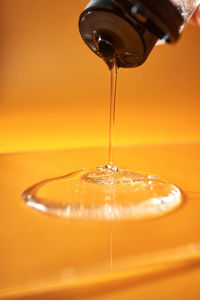 A drop of body gel or shampoo pouring from above on a yellow saturated background.