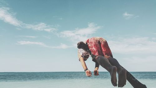 Woman with arms raised on beach against sky