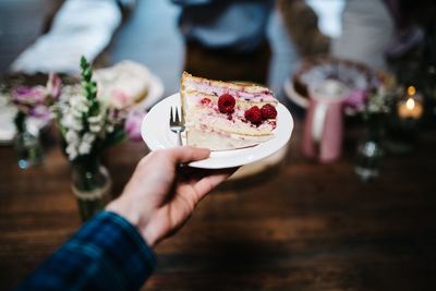 Close-up of cropped hand holding cake slice in plate