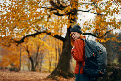 Young woman standing by tree during autumn