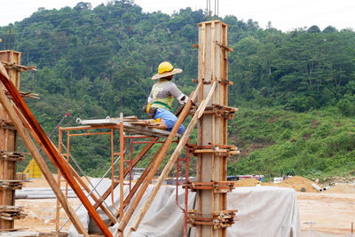 Rear view of man working on plants against trees