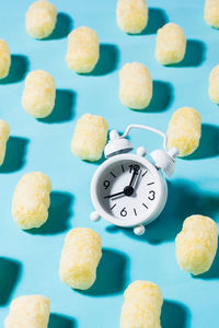 A trending background of corn sticks and an alarm clock on a blue backdrop in harsh light.
