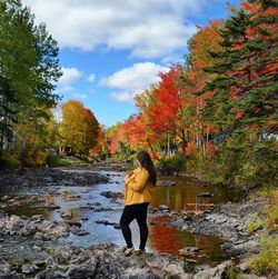 Woman looking away while standing by stream during autumn 