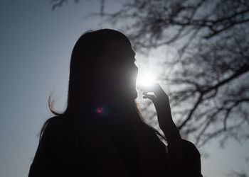 Silhouette woman standing by bare tree against sky