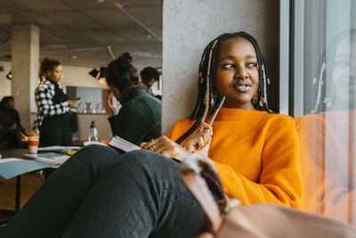 Thoughtful young woman sitting with book in university cafeteria