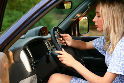 Young woman talking on a cell phone while sitting in the car in the driver's seat. attractive blonde 