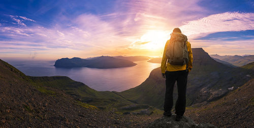 Rear view of man standing on mountain against sky during sunset