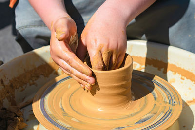 Child's hands making a clay vase behind a potter's wheel