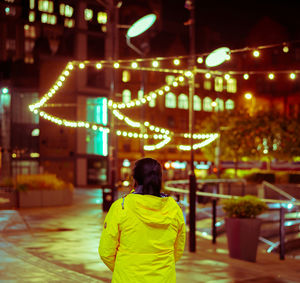 Rear view of woman standing against illuminated lights at night