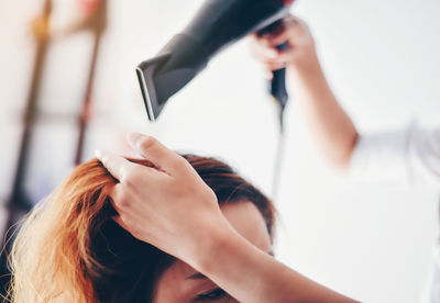 Cropped hand of beautician straightening woman hair in hair salon