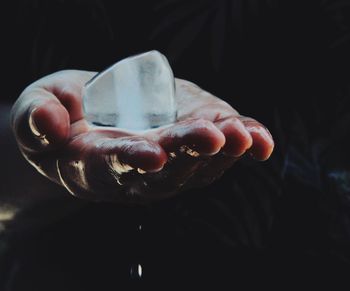 Close-up of cropped hand holding ice against black background