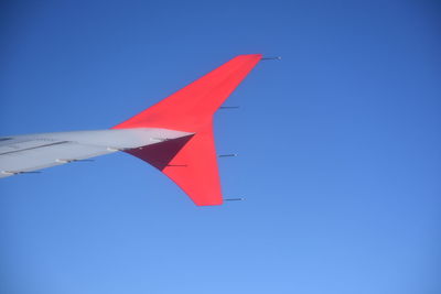 Low angle view of airplane wing against clear blue sky