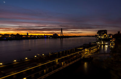 Illuminated bridge over river against sky at sunset