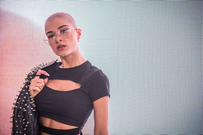 Portrait of young woman with shaved head standing against abstract backgrounds