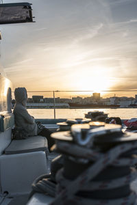 Side view of woman sitting on seat in boat against sky during sunset