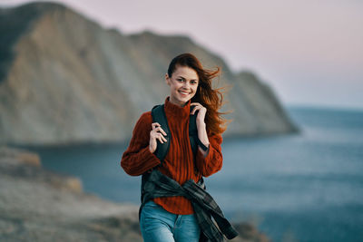 Portrait of smiling young woman standing against sea