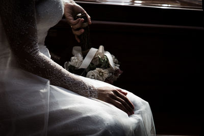 Midsection of bride holding bouquet while sitting by table at wedding ceremony