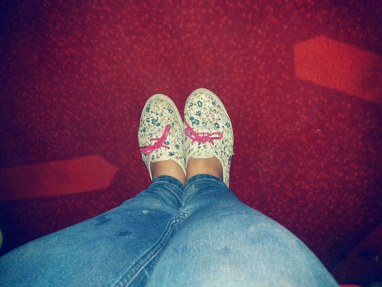 LOW SECTION OF WOMAN WEARING CANVAS SHOES STANDING ON RED FLOOR