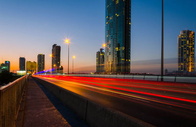 Light trails on road by buildings against sky in city