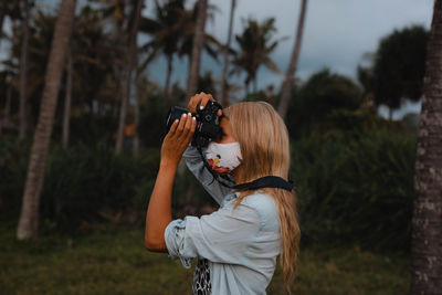 Man photographing woman standing by tree against plants