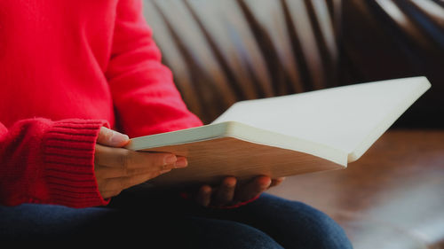 Midsection of woman reading book while sitting on sofa at home