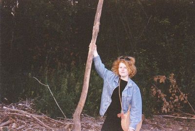 Full length of woman standing by tree trunk in forest