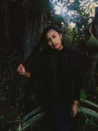 Beautiful young woman standing by tree trunk in forest