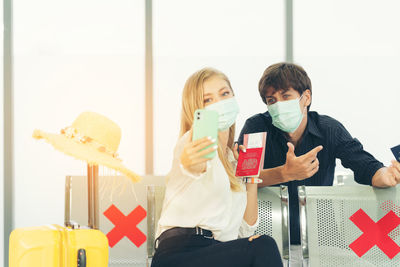 Young women play selfie woth smartphone traveler in protective mask holds passport during affected