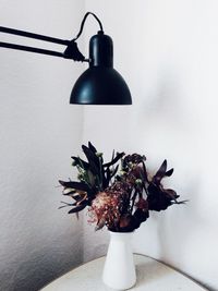 Flower vase below electric lamp against wall