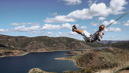 Man in mid-air by mountains against sky