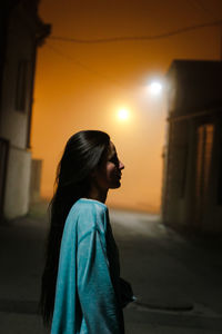 Profile view of young woman standing on road in city at night