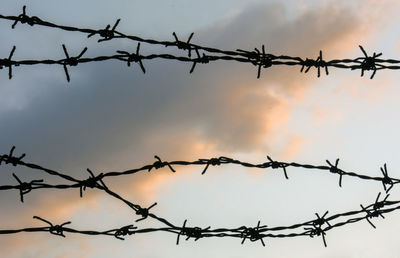 Low angle view of barbed wire against sky during sunset