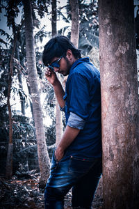 Man standing by tree trunk in forest