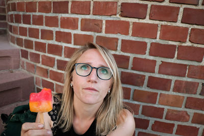 Woman holding ice cream against brick wall