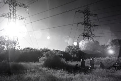 People on field by electricity pylon against sky