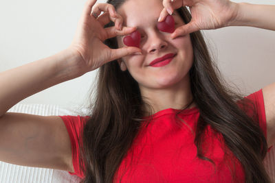 Close-up of cheerful woman holding heart shape candies over face