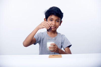 Young woman using phone while sitting on table against white background