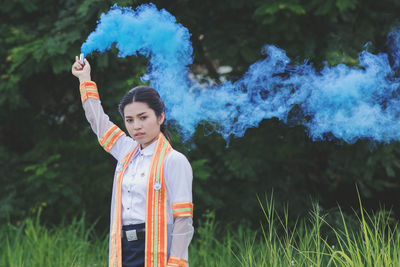 Portrait of woman holding distress flare while standing on field