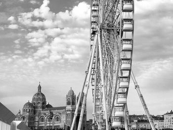 Ferris wheel in city against cloudy sky