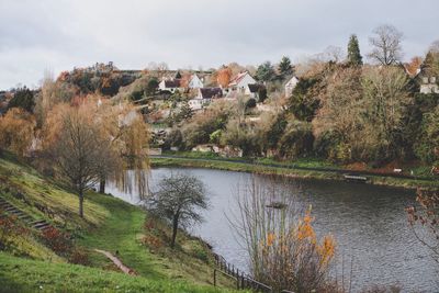 Scenic view of lake by trees and houses against sky