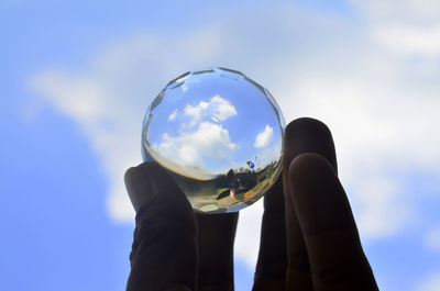 Low angle view of hand holding crystal ball against sky