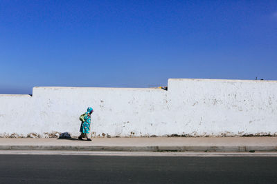 Rear view of man against white wall against clear blue sky