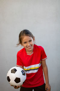 Portrait of smiling girl holding soccer ball against white background