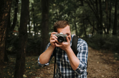 Young man photographing camera in forest