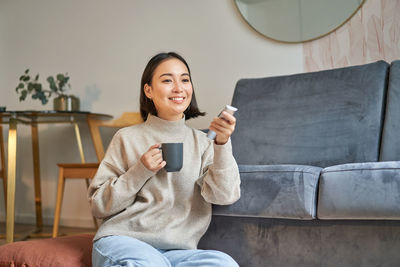 Young woman using mobile phone while sitting on sofa at home