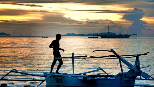 Silhouette man standing on sea against sky during sunset