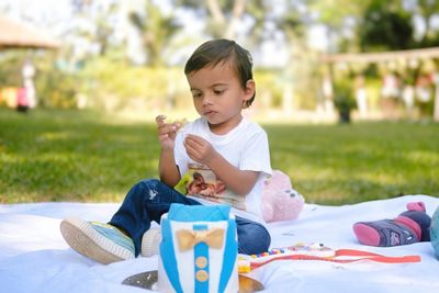 Side view of young woman drinking beer while sitting on picnic blanket at park