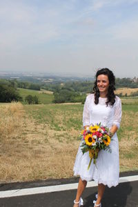 Portrait of smiling young woman standing on field against sky