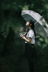 Side view of woman holding umbrella while standing in forest during rainy season