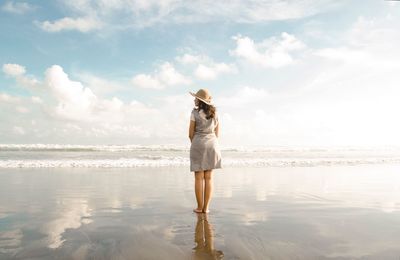 Rear view of woman standing at beach against sky